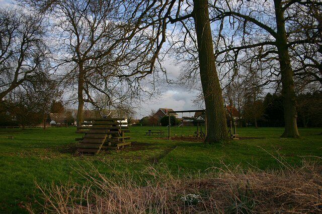 A park with a wooden structure, trees, and a distant building.