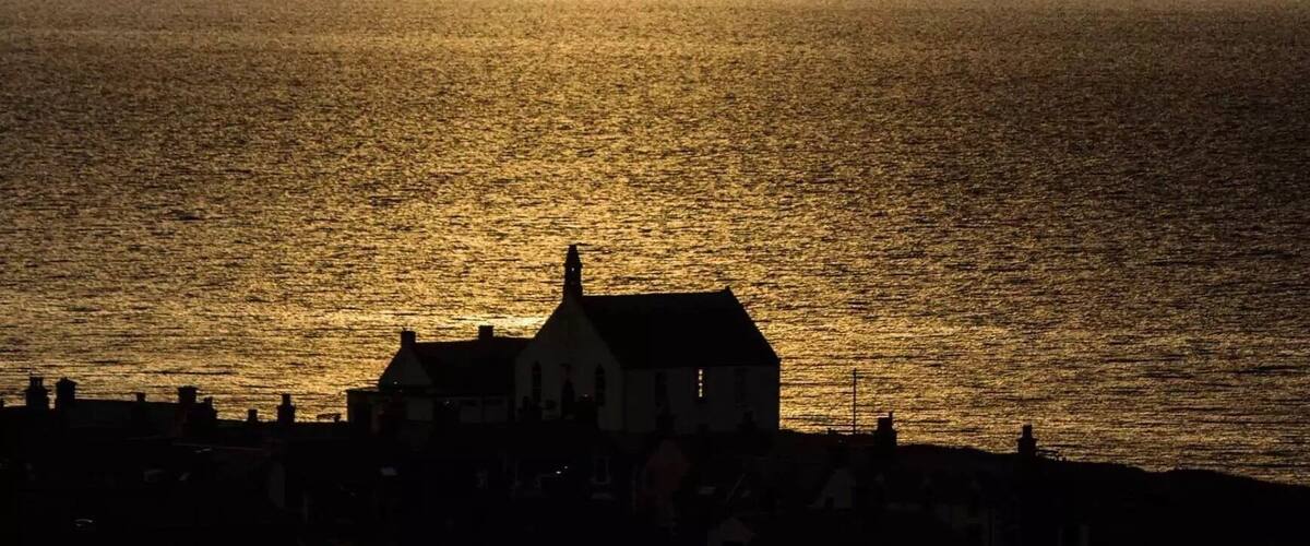 A coastal sunset with a silhouette of a house and buildings against the sky.
