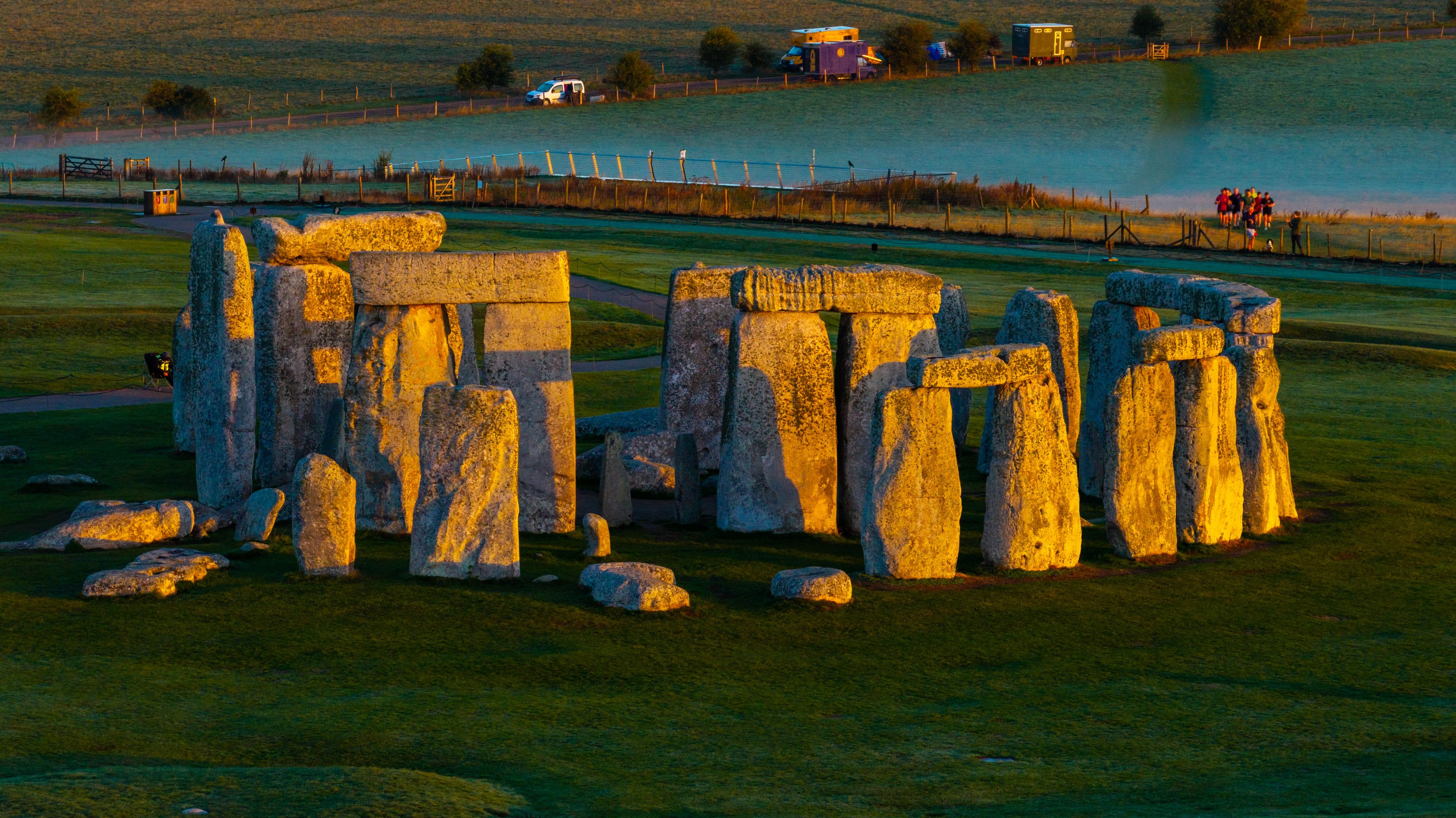 Aerial view of Stonehenge illuminated by the warm golden light of sunrise, surrounded by the lush green landscape of the Salisbury Plain in Salisbury, England, United Kingdom.