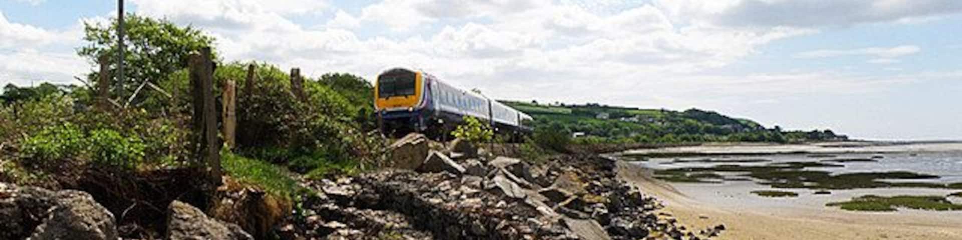 Railway by the Sea A Class 175 DMU heads north for Carmarthen after stopping at Ferryside, seen in the distance. The railway here runs alongside the River Towy as it flows into the sea.