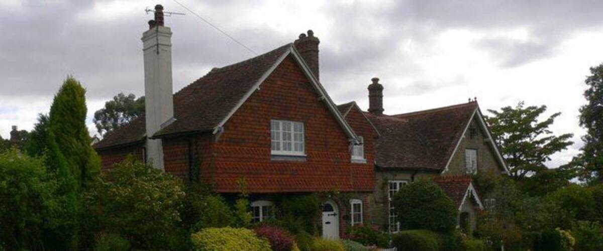A traditional brick house with a red-tiled roof, surrounded by lush greenery and a well-maintained lawn.