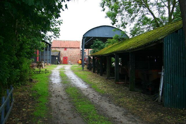 A rural farm with a dirt path leading to a barn, surrounded by green fields and trees.