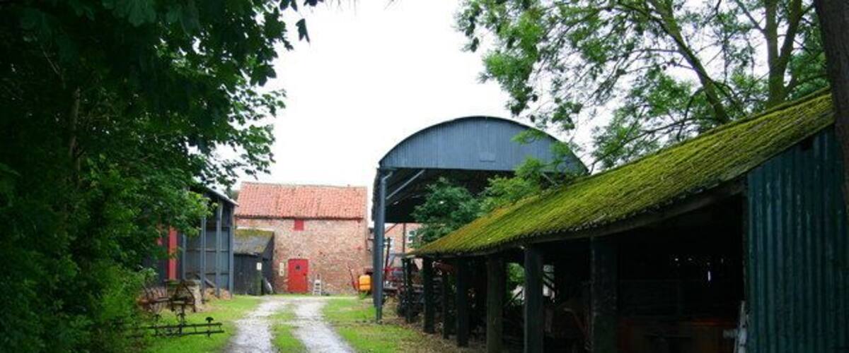 A rural farm with a dirt path leading to a barn, surrounded by green fields and trees.