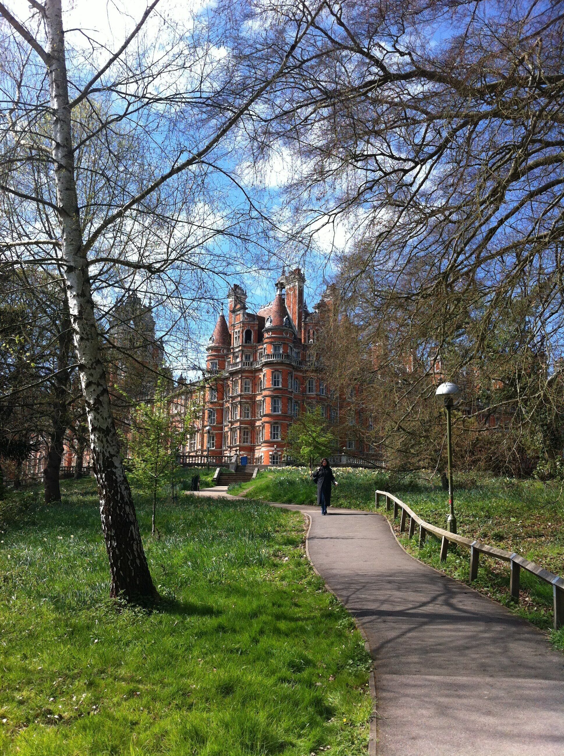 A park pathway leading to a large, ornate building with multiple towers and turrets.