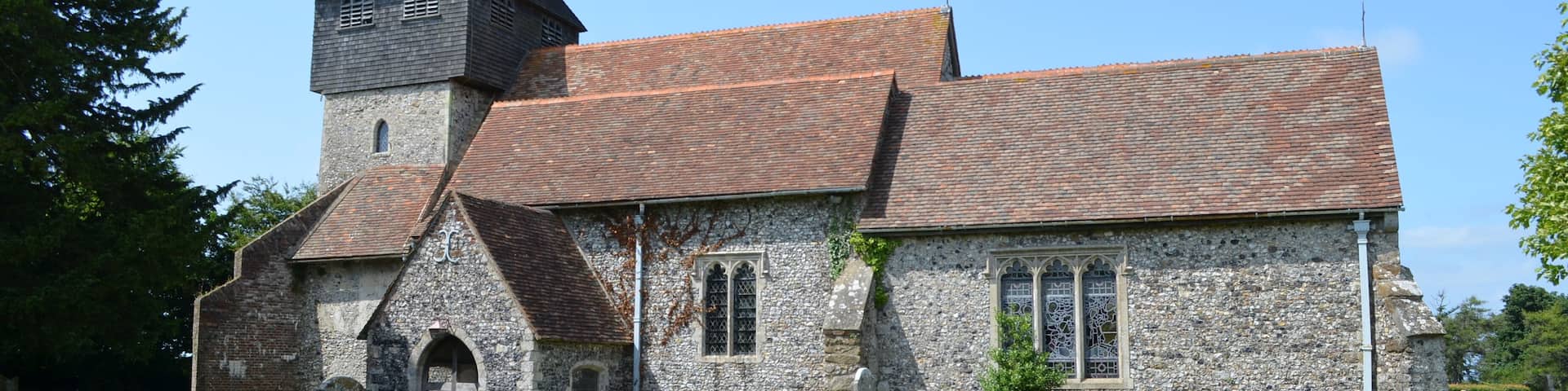 The church dates from the late 11th century onwards and was restored in 1877 by Ewan Christian. It is built with knapped flint and stone dressings with tiled roofs. There is a west tower, nave with north and south aisles, south porch and chancel with north and south chapels. The tower is from the 13th century with an earlier base. In the 14th century a square timber framed belfry with a short spire was built to form the second stage of the tower. it is heavily buttressed. There are six bells. The nave is continuous with the south wall of the tower, and follows the outline of the original Norman nave. Originally there were no side aisles or chapels and the chancel would have been much shorter. The south aisle dates from the 14th century with earlier origins. It has a 15th century crown post roof. Both aisles are from an early date, possibly before 1200. They were probably added as part of the building programme by Saint Gregory's Priory. The arcades were rebuilt in the 14th century in the Perpendicular style with octagonal piers. The north Chapel was built soon after 1300 and the east window is contemporary with this date. The south Chapel, dedicated to St John the Baptist, is probably a similar date. In the 15th century several wills bequeathed money for repairs. The south Chapel is also known as the Honywood Chapel as there is a monument to Sir Thomas Honywood, died 1622. The style closely resembles the work of Nicholas Stone, although unsigned. There is also a monument to Sir William Honywood, died 1669. Sir William was master of the society of silk merchants and died in his 81st year. His second wife Lady Dorothy Honywood whose monument is nearby died within four months of her husband. There are other dedications to the Honywood's in floor ledgers and monuments. The chancel is Early English and was lengthened in the 13th century replacing the Norman one. The chancel arch was rebuilt in the 14th century. The chancel contains a piscina. The font bowl is from the 12th century made of Purbeck marble and supported on modern shafts. The church was restored in 1877, it was in need of urgent attention and was described as being "in a damp and miserable condition". Box pews were removed, choir stalls were placed in the chancel and the altar platform was extended. The roof of the Honywood Chapel was rebuilt, paid for by the Honywood family. Most of the money for the rest of the repairs was from public subscription.