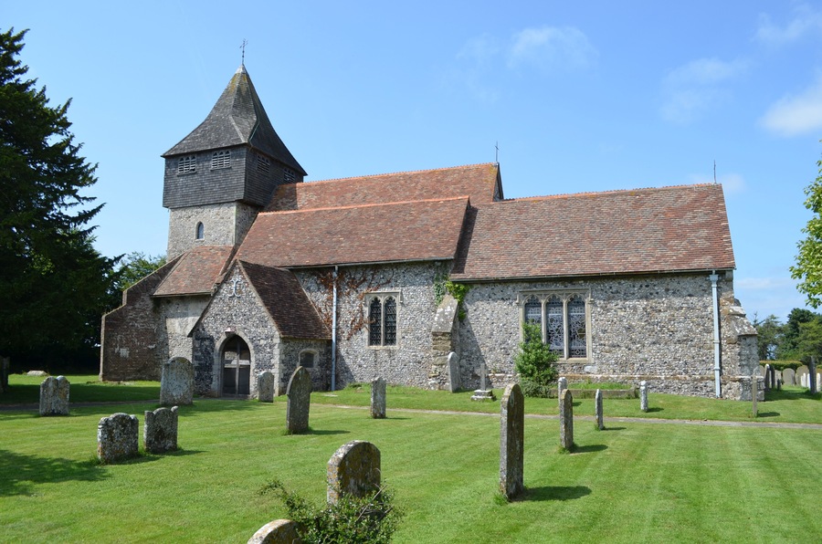 The church dates from the late 11th century onwards and was restored in 1877 by Ewan Christian. It is built with knapped flint and stone dressings with tiled roofs. There is a west tower, nave with north and south aisles, south porch and chancel with north and south chapels. The tower is from the 13th century with an earlier base. In the 14th century a square timber framed belfry with a short spire was built to form the second stage of the tower. it is heavily buttressed. There are six bells. The nave is continuous with the south wall of the tower, and follows the outline of the original Norman nave. Originally there were no side aisles or chapels and the chancel would have been much shorter. The south aisle dates from the 14th century with earlier origins. It has a 15th century crown post roof. Both aisles are from an early date, possibly before 1200. They were probably added as part of the building programme by Saint Gregory's Priory. The arcades were rebuilt in the 14th century in the Perpendicular style with octagonal piers. The north Chapel was built soon after 1300 and the east window is contemporary with this date. The south Chapel, dedicated to St John the Baptist, is probably a similar date. In the 15th century several wills bequeathed money for repairs. The south Chapel is also known as the Honywood Chapel as there is a monument to Sir Thomas Honywood, died 1622. The style closely resembles the work of Nicholas Stone, although unsigned. There is also a monument to Sir William Honywood, died 1669. Sir William was master of the society of silk merchants and died in his 81st year. His second wife Lady Dorothy Honywood whose monument is nearby died within four months of her husband. There are other dedications to the Honywood's in floor ledgers and monuments. The chancel is Early English and was lengthened in the 13th century replacing the Norman one. The chancel arch was rebuilt in the 14th century. The chancel contains a piscina. The font bowl is from the 12th century made of Purbeck marble and supported on modern shafts. The church was restored in 1877, it was in need of urgent attention and was described as being "in a damp and miserable condition". Box pews were removed, choir stalls were placed in the chancel and the altar platform was extended. The roof of the Honywood Chapel was rebuilt, paid for by the Honywood family. Most of the money for the rest of the repairs was from public subscription.