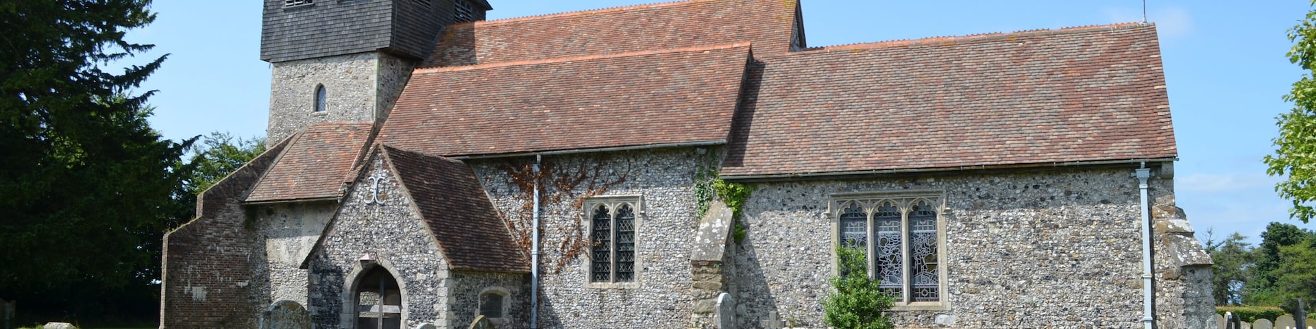 The church dates from the late 11th century onwards and was restored in 1877 by Ewan Christian. It is built with knapped flint and stone dressings with tiled roofs. There is a west tower, nave with north and south aisles, south porch and chancel with north and south chapels. The tower is from the 13th century with an earlier base. In the 14th century a square timber framed belfry with a short spire was built to form the second stage of the tower. it is heavily buttressed. There are six bells. The nave is continuous with the south wall of the tower, and follows the outline of the original Norman nave. Originally there were no side aisles or chapels and the chancel would have been much shorter. The south aisle dates from the 14th century with earlier origins. It has a 15th century crown post roof. Both aisles are from an early date, possibly before 1200. They were probably added as part of the building programme by Saint Gregory's Priory. The arcades were rebuilt in the 14th century in the Perpendicular style with octagonal piers. The north Chapel was built soon after 1300 and the east window is contemporary with this date. The south Chapel, dedicated to St John the Baptist, is probably a similar date. In the 15th century several wills bequeathed money for repairs. The south Chapel is also known as the Honywood Chapel as there is a monument to Sir Thomas Honywood, died 1622. The style closely resembles the work of Nicholas Stone, although unsigned. There is also a monument to Sir William Honywood, died 1669. Sir William was master of the society of silk merchants and died in his 81st year. His second wife Lady Dorothy Honywood whose monument is nearby died within four months of her husband. There are other dedications to the Honywood's in floor ledgers and monuments. The chancel is Early English and was lengthened in the 13th century replacing the Norman one. The chancel arch was rebuilt in the 14th century. The chancel contains a piscina. The font bowl is from the 12th century made of Purbeck marble and supported on modern shafts. The church was restored in 1877, it was in need of urgent attention and was described as being "in a damp and miserable condition". Box pews were removed, choir stalls were placed in the chancel and the altar platform was extended. The roof of the Honywood Chapel was rebuilt, paid for by the Honywood family. Most of the money for the rest of the repairs was from public subscription.