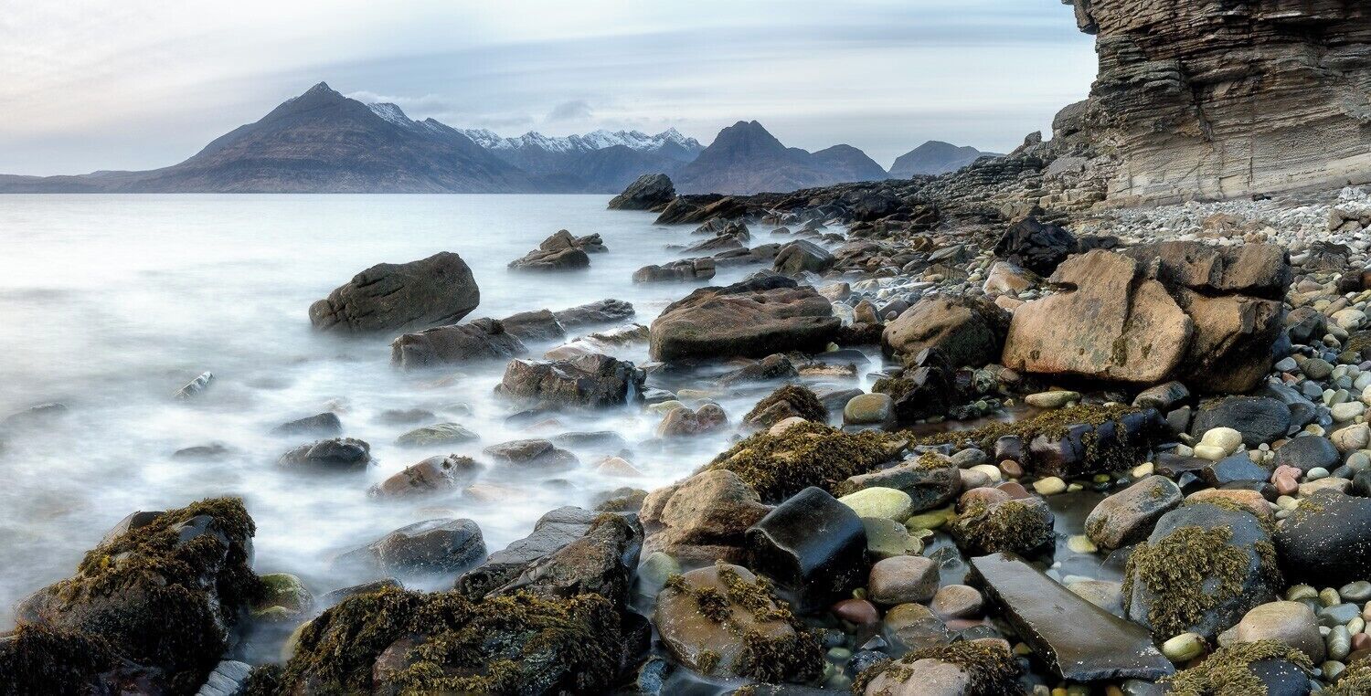 A rocky shoreline with a calm sea and distant mountains.