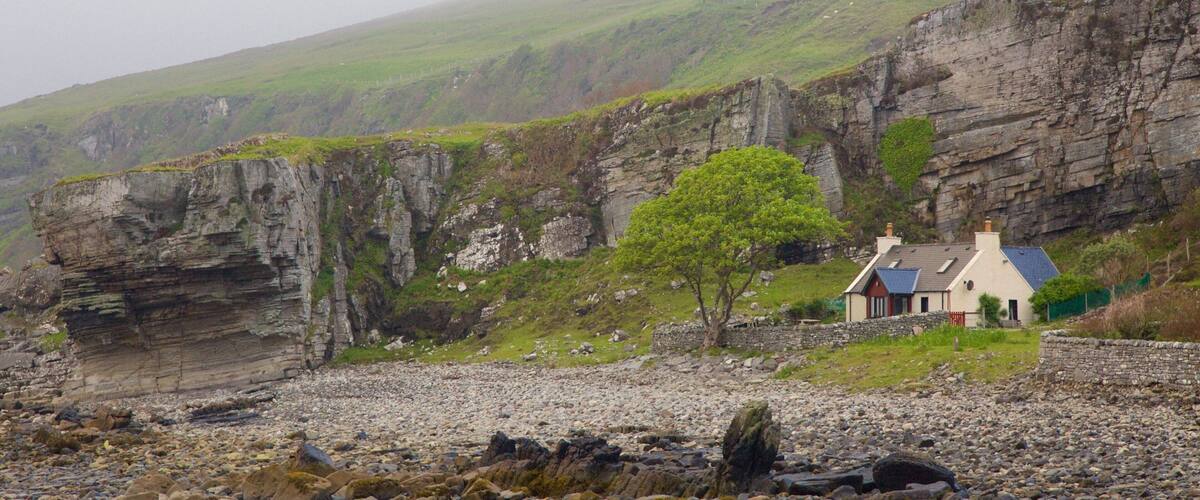 A coastal landscape with a rocky cliff, a small house, and a tree.