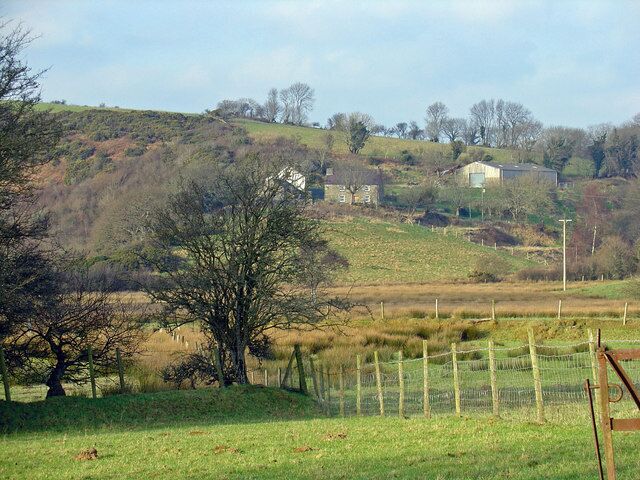 A rural landscape with rolling hills, a fenced field, and scattered trees.