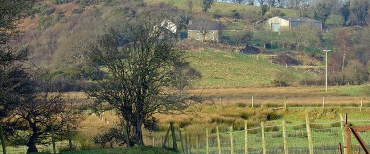 A rural landscape with rolling hills, a fenced field, and scattered trees.