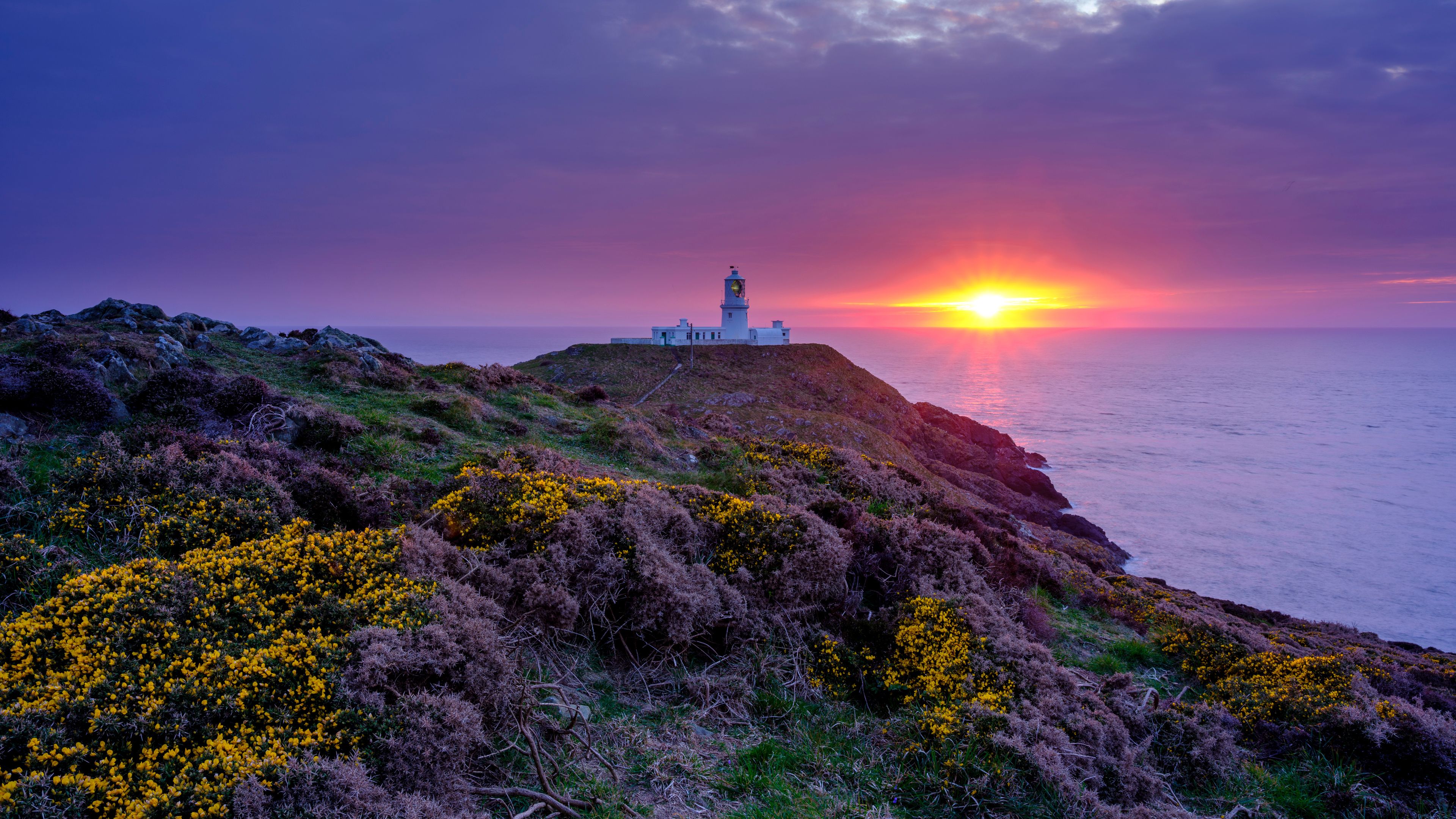 A lighthouse on a rocky cliff overlooking the ocean at sunset.
