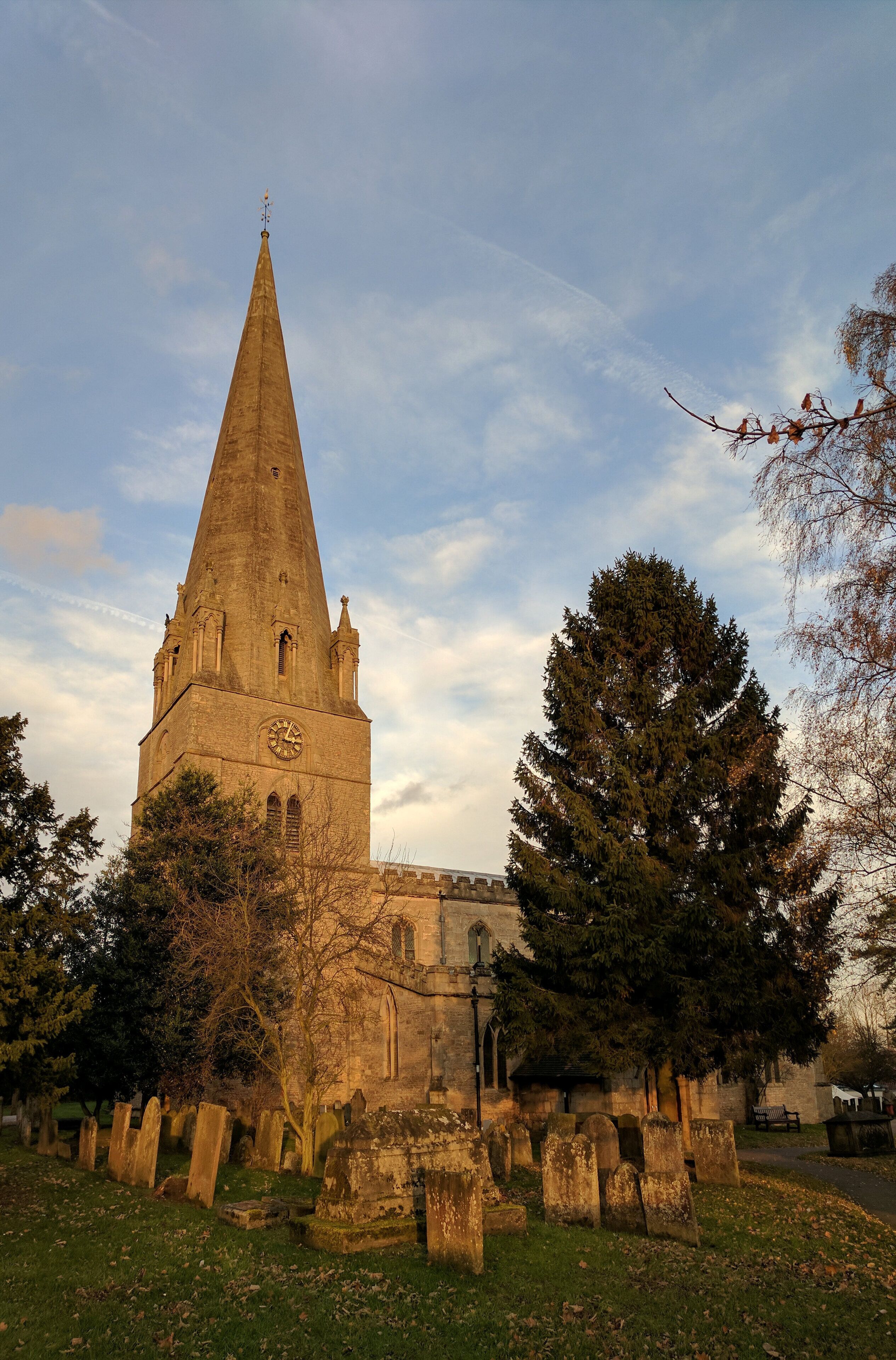 A church with a tall spire, surrounded by trees and gravestones.
