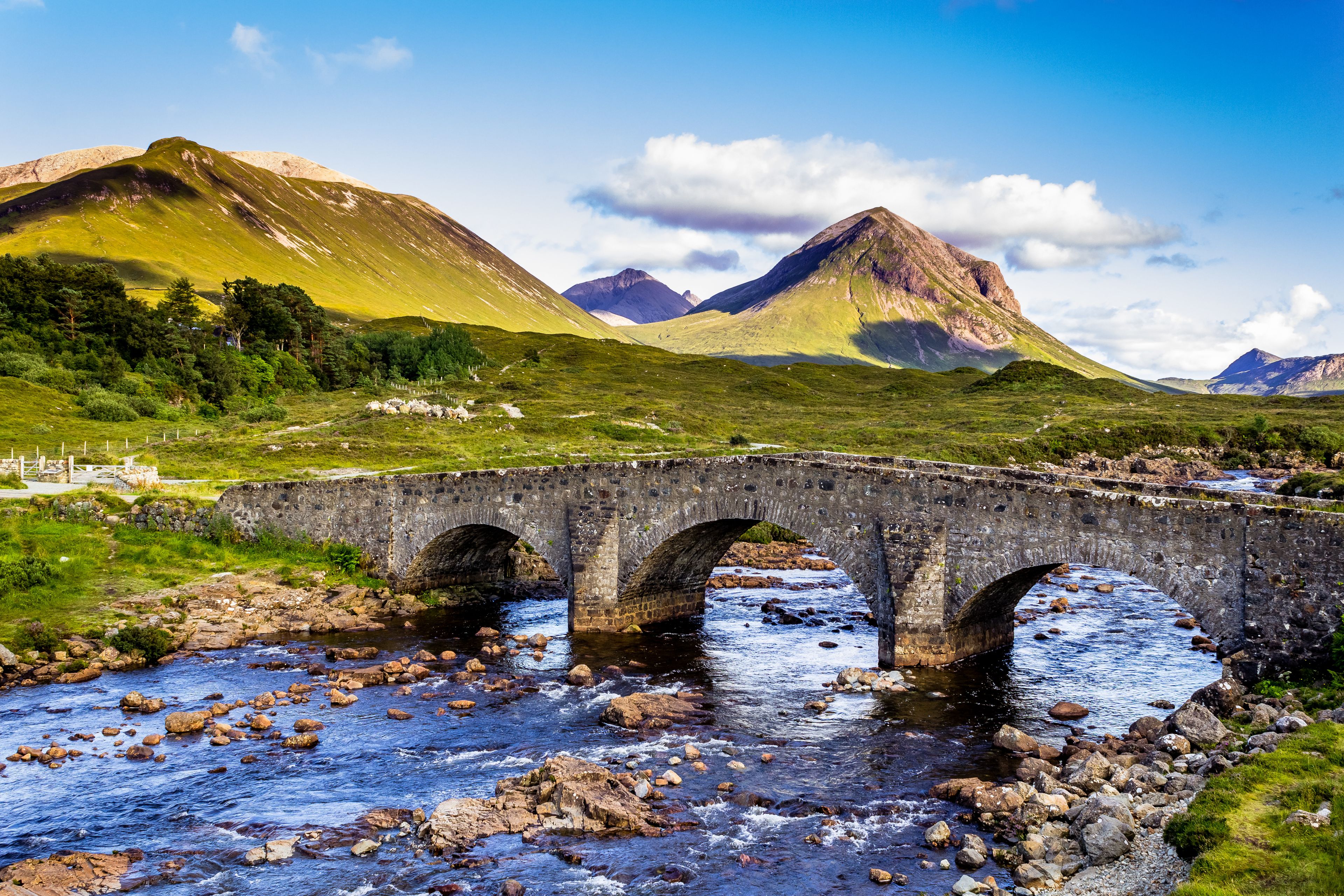 Un pont de pierre enjambant une rivière, avec des montagnes en arrière-plan.