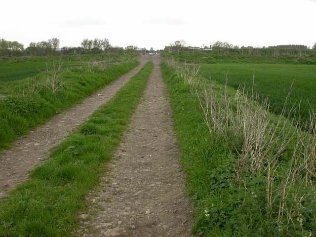 Track to Sewage Works. Another track crosses at right angles on the small rise ahead. Some vehicles and buildings connected with the sewage works can be seen behind it.