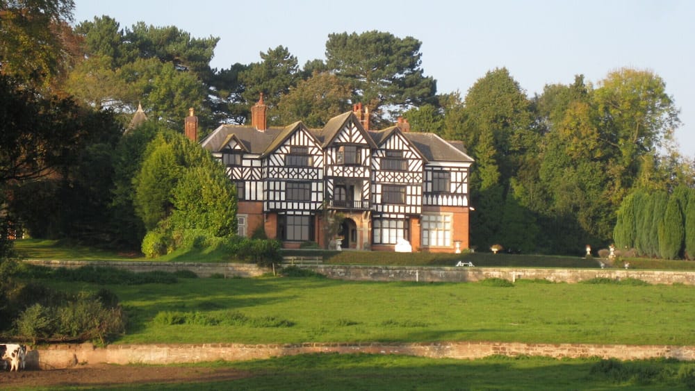 A Tudor-style house with a large garden and a pond.