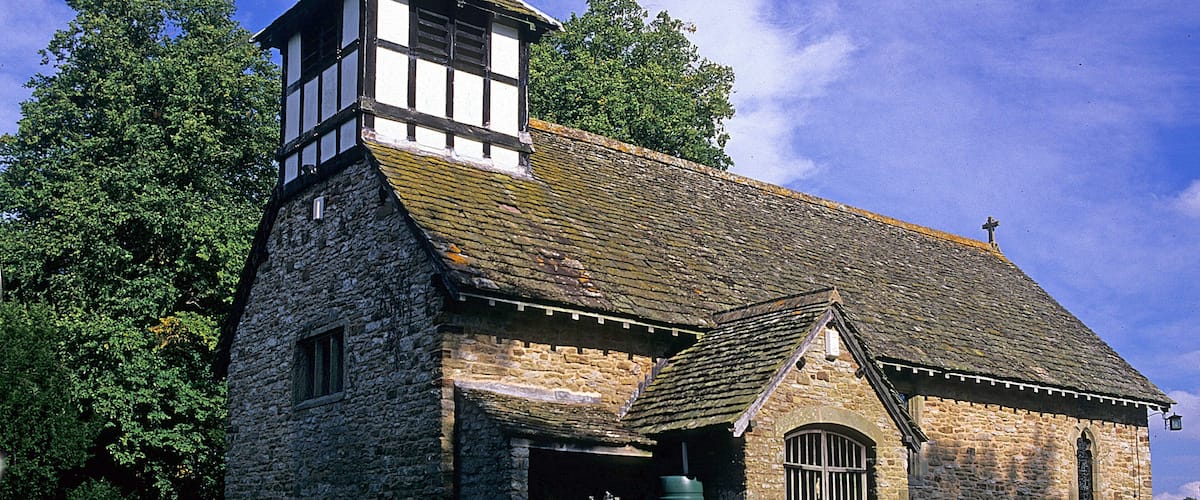 A stone church with a bell tower and a large tree in the foreground.