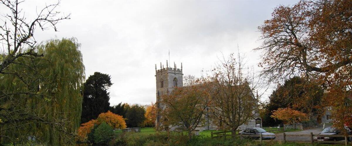 A calm river with autumn foliage, a historic tower, and a park with trees and a car.