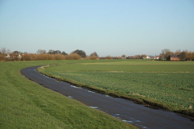A winding road through a green field with a small stream running alongside it.