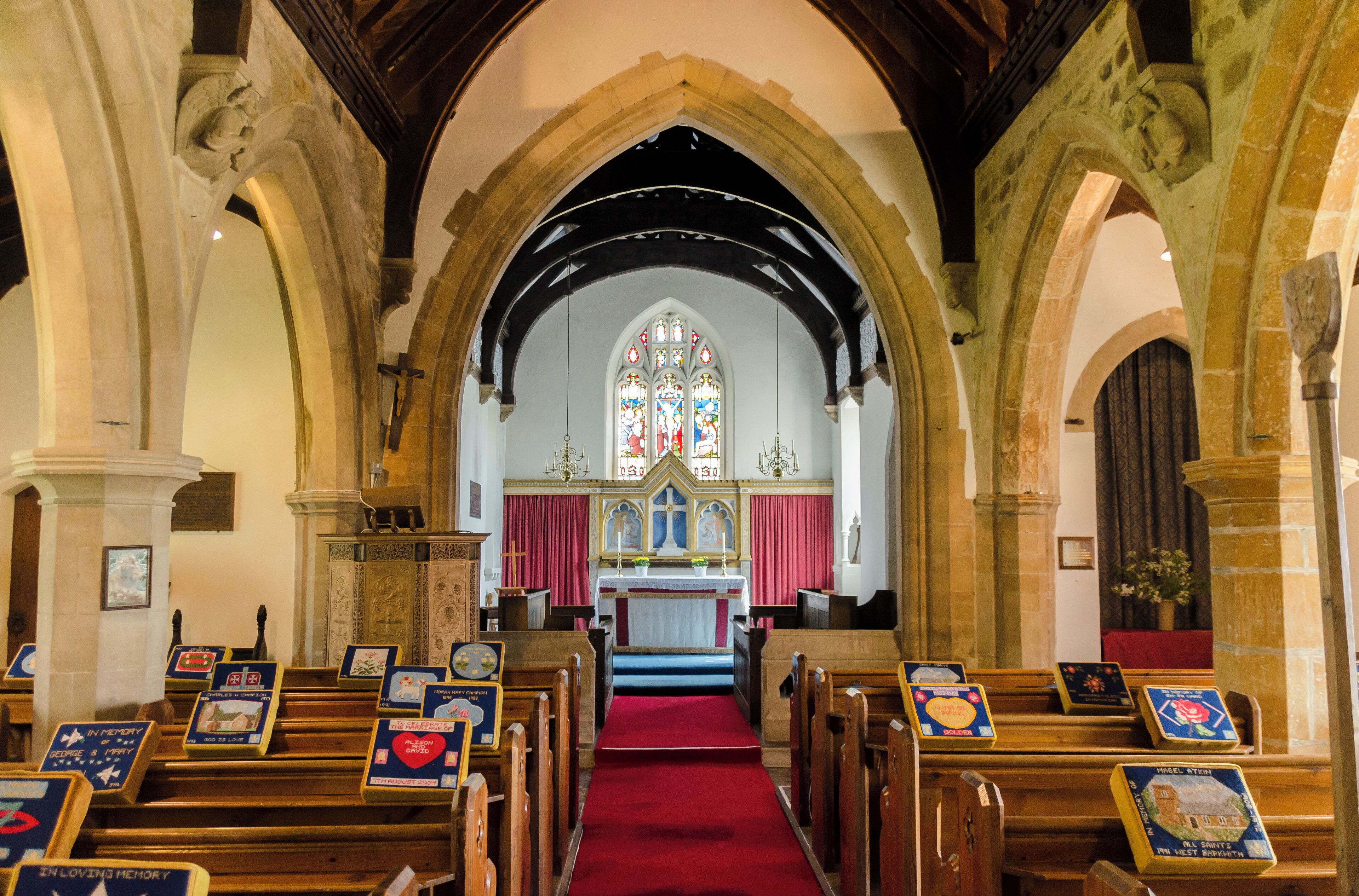 An interior of a church with wooden pews, a red carpet, and stained glass windows.