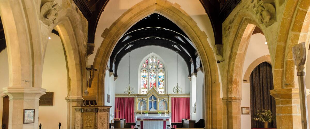 An interior of a church with wooden pews, a red carpet, and stained glass windows.