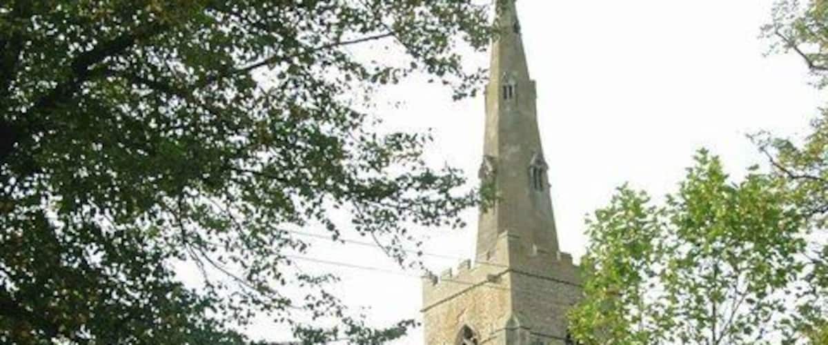 A church with a tall spire, surrounded by trees and a stone wall.