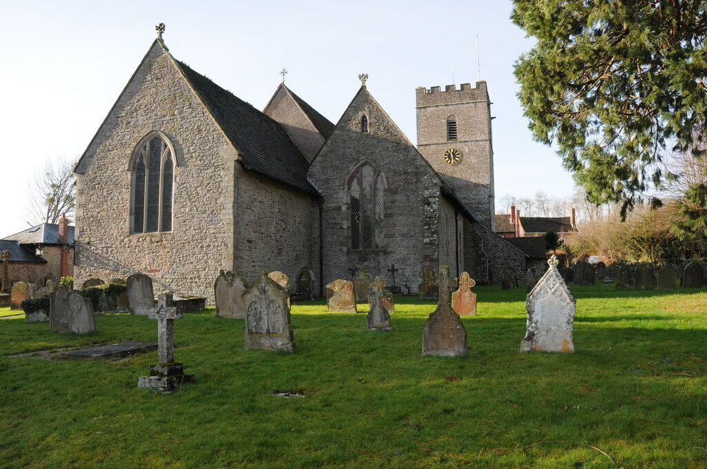 A stone church with a tall tower and a graveyard in front.