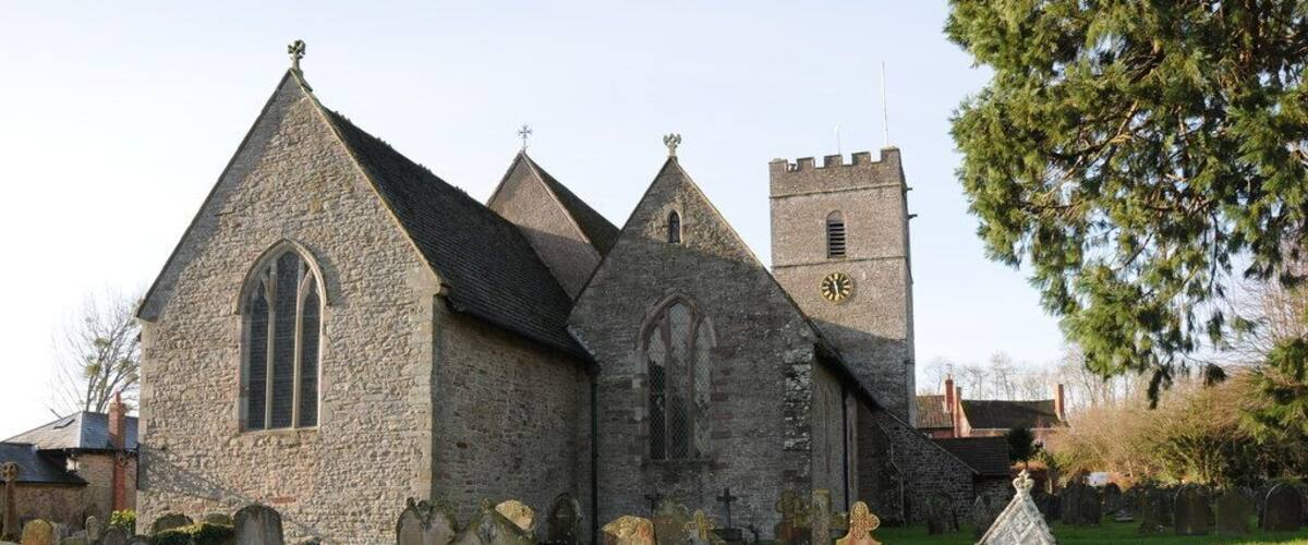 A stone church with a tall tower and a graveyard in front.