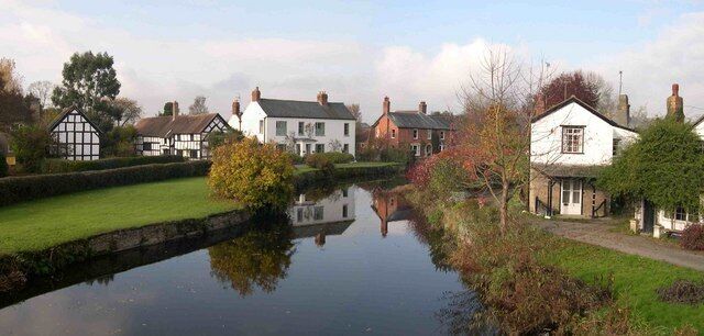 A calm river with houses on one side and a grassy area with trees on the other.