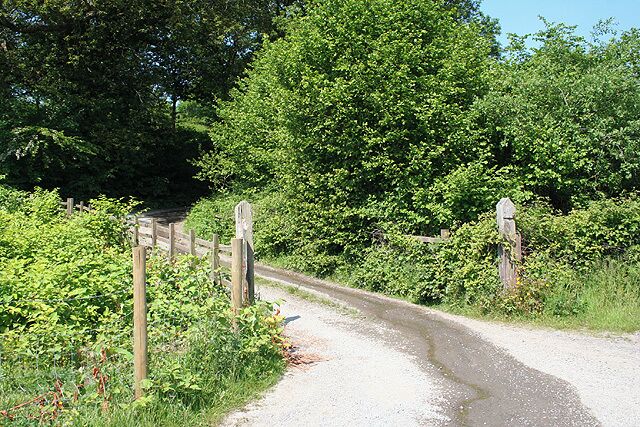 A gravel road curving through a wooded area with a wooden gate and directional signposts.