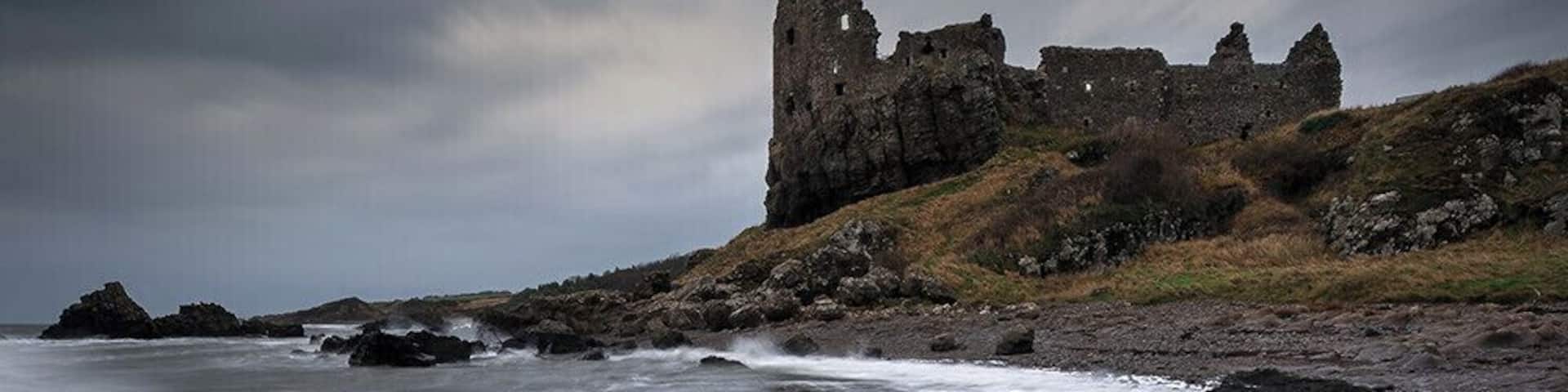 A coastal landscape with a ruined castle and turbulent sea.