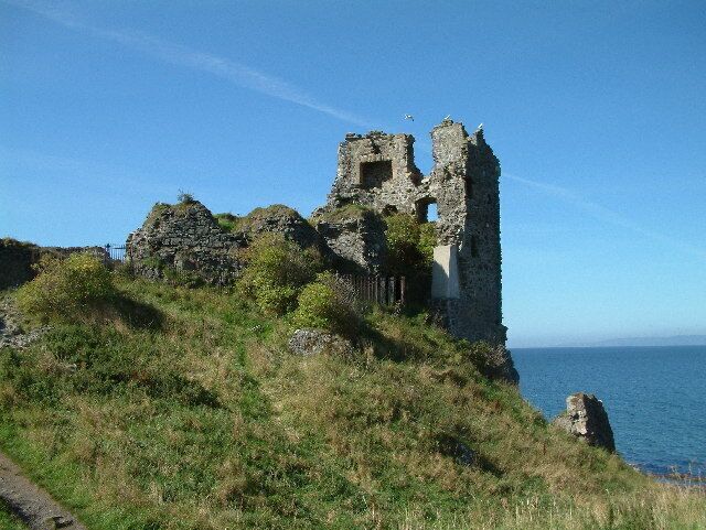 A coastal ruin with a tower and walls, surrounded by grass and overlooking the sea.