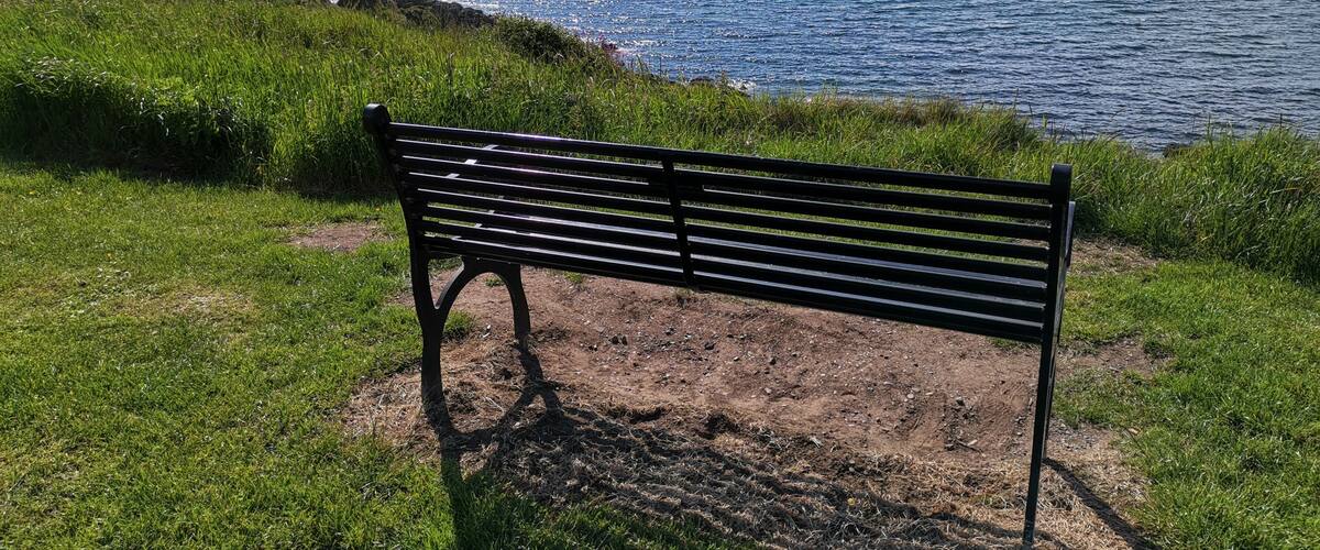 A bench overlooking a coastal landscape with a view of the sea and distant hills.