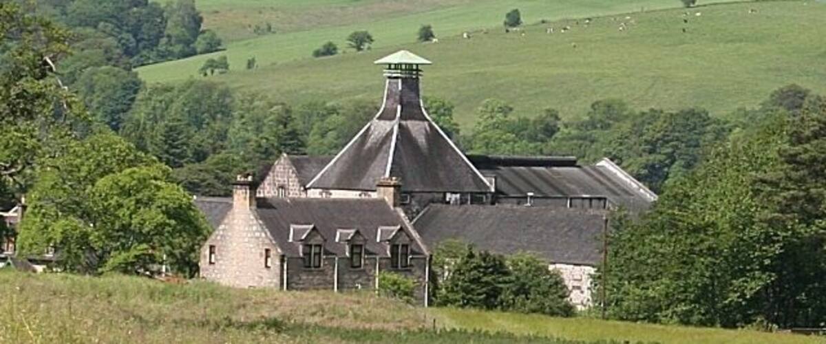 A large stone building with a conical roof, surrounded by lush green fields and rolling hills.