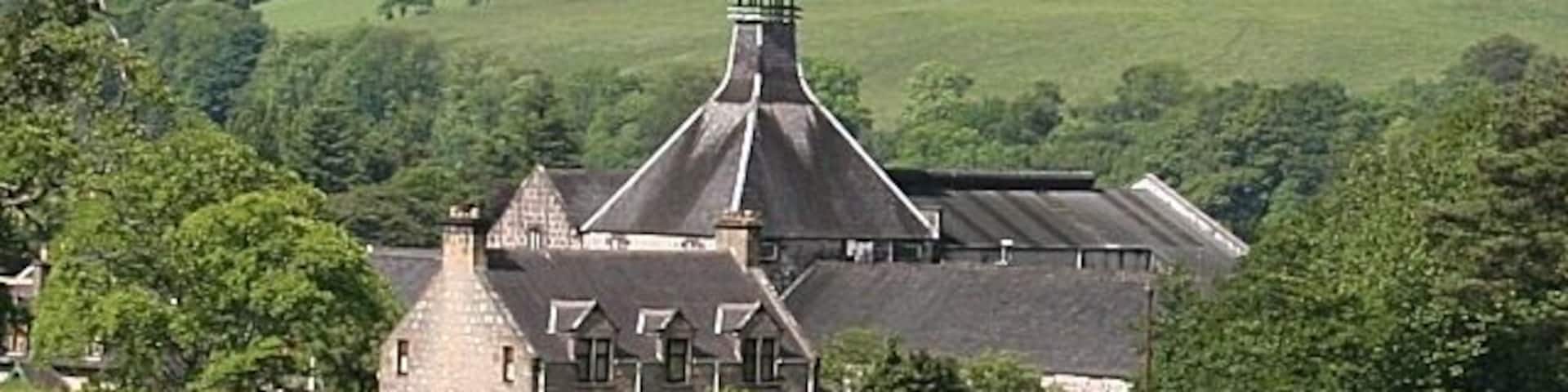 A large stone building with a conical roof, surrounded by lush green fields and rolling hills.
