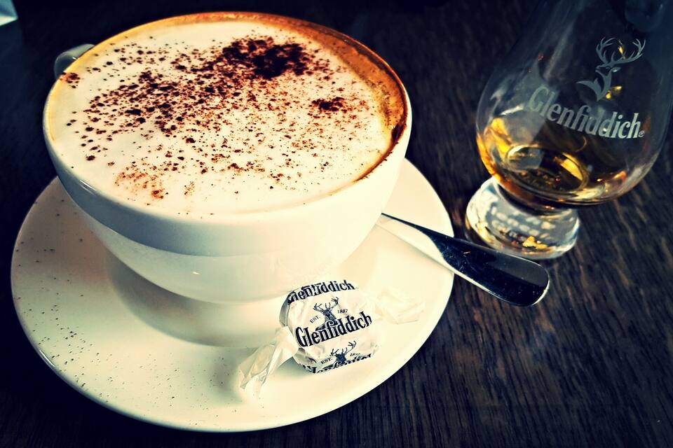 Una tassa de cafè amb escuma, un got de whisky Glenfiddich i un paquet de whisky sobre un calvari.