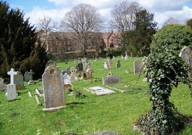 A cemetery with numerous headstones and crosses, surrounded by grass and trees.