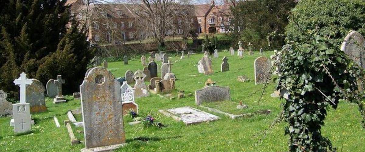 A cemetery with numerous headstones and crosses, surrounded by grass and trees.