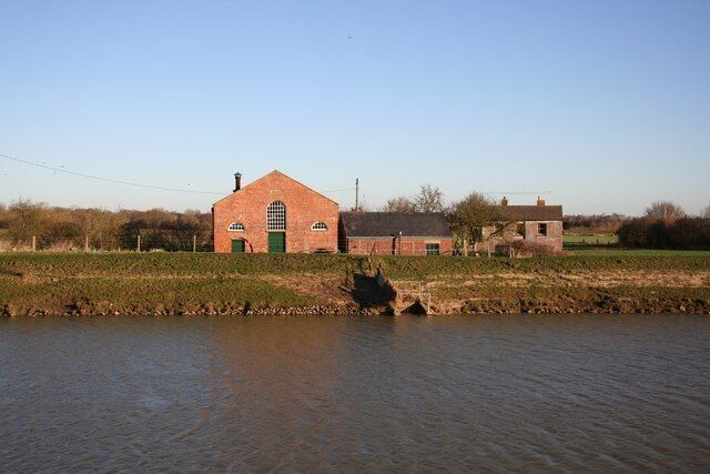 A brick building with a green door, a field, and a body of water.