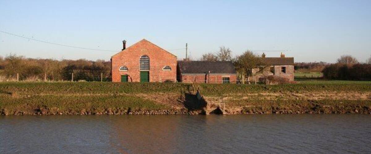 A brick building with a green door, a field, and a body of water.