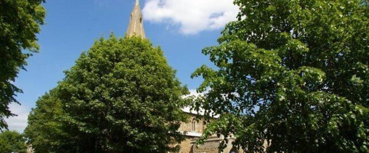 A church with a tall spire, surrounded by trees and a stone wall.
