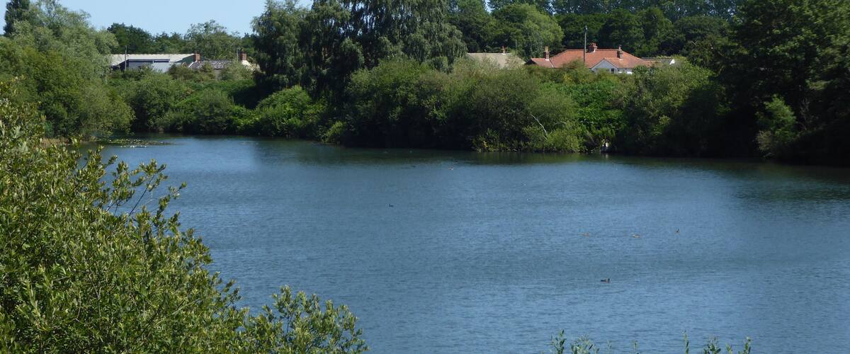 A calm river surrounded by dense greenery and houses with red roofs.