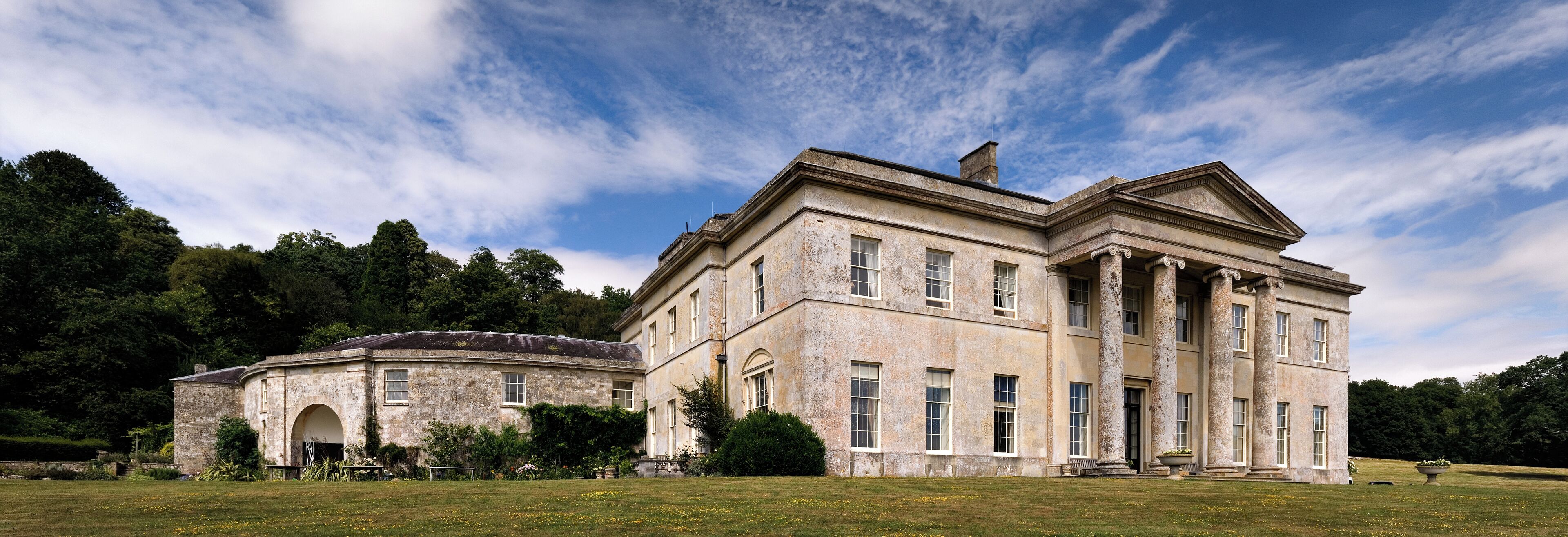 A large, historic building with classical architecture, surrounded by a well-maintained lawn and trees.