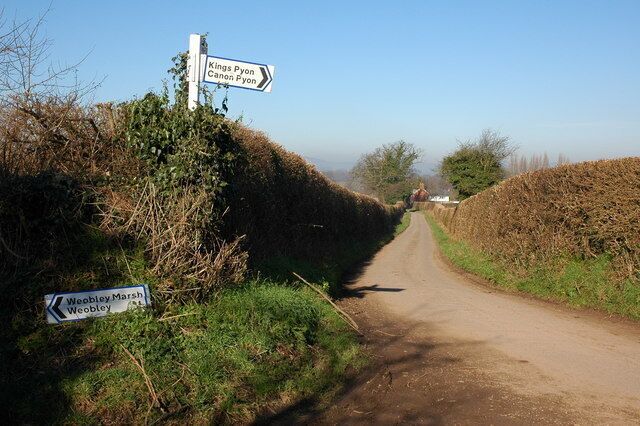 Una carretera rural con señales que indican Kings Pyne y Weobley Marsh.