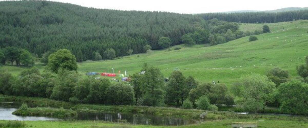 A green field with a pond, trees, and a red building in the distance.