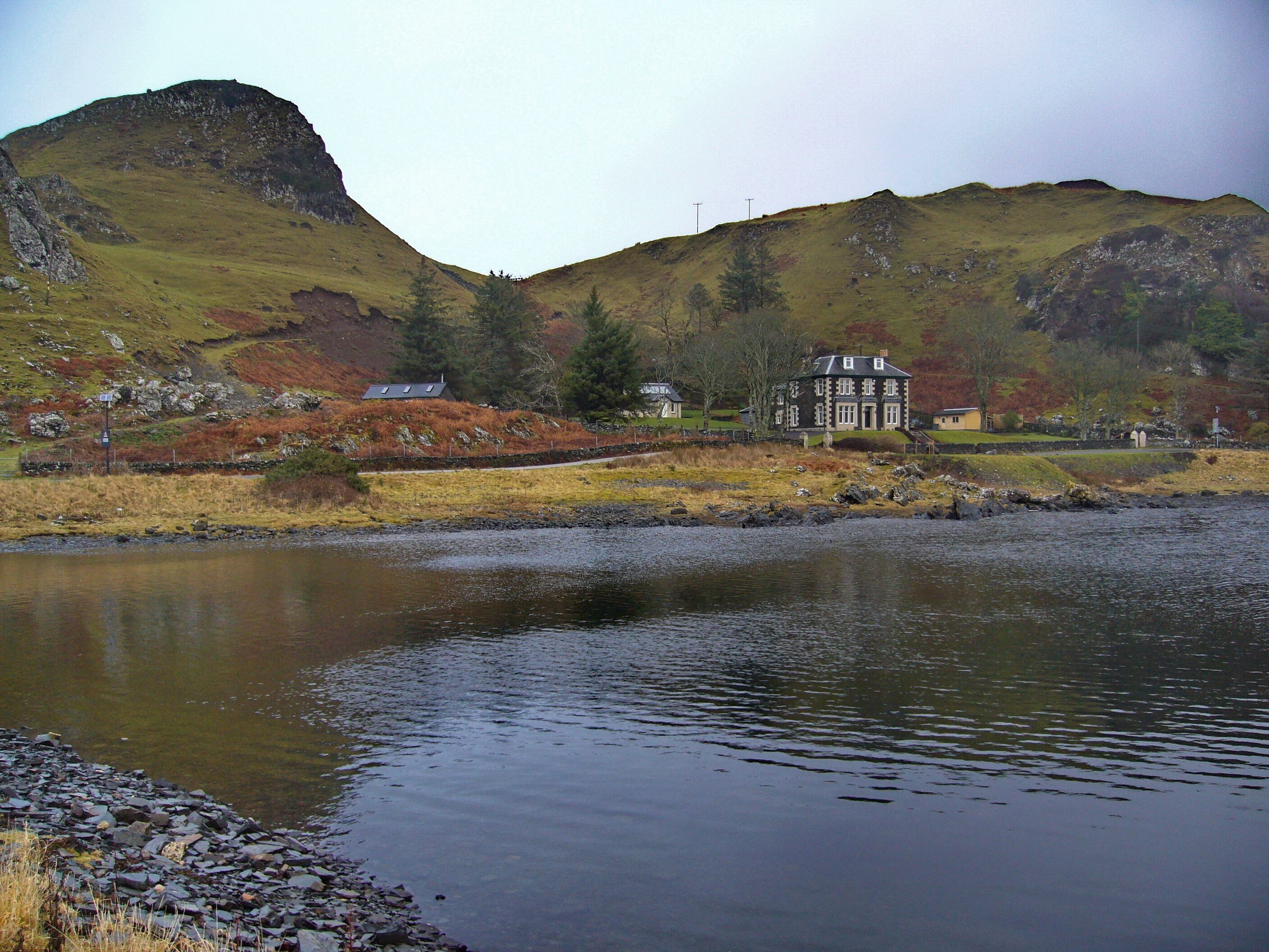 A lake with a house on a hillside and a mountain in the background.