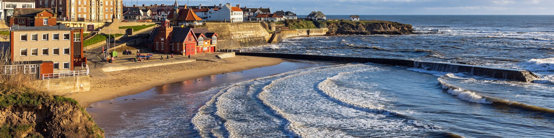 A coastal town with a sandy beach, a sea wall, and buildings along the shore.