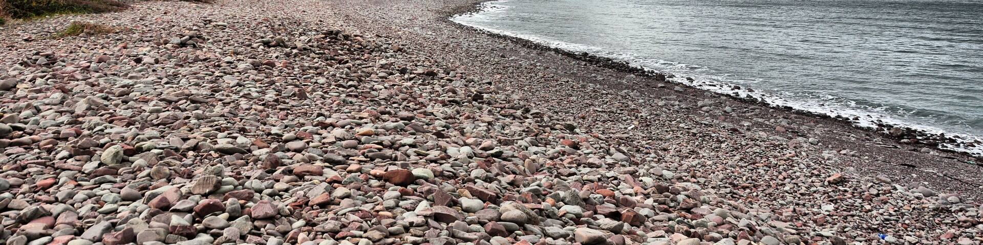 A pebbly beach with a forested hillside and a distant mountain.