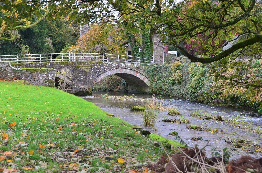 A stone bridge over a river, surrounded by greenery and autumn leaves.