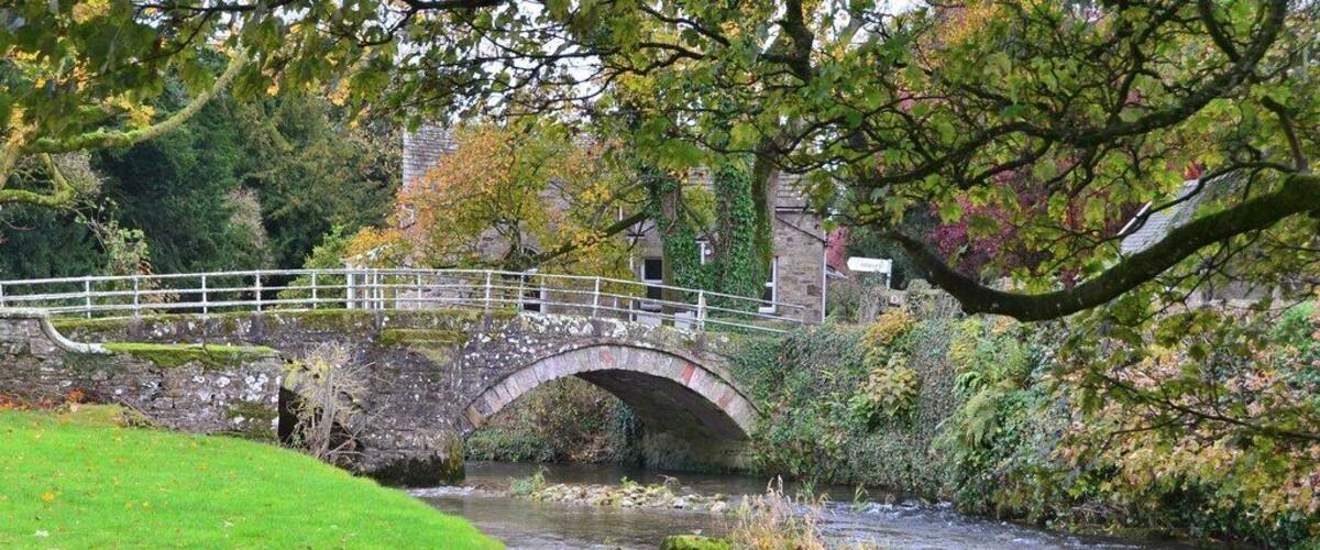 A stone bridge over a river, surrounded by greenery and autumn leaves.
